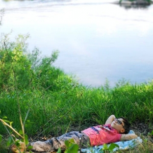 Zdjęcie chłopca leżącego wśród trawy nad brzegiem wody